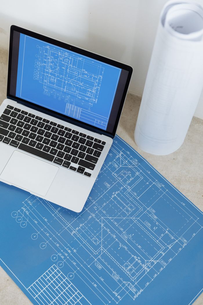 Mastering the First Impression: Your intriguing post title goes here Laptop showing engineering blueprint with rolled paper and drawings on table.
